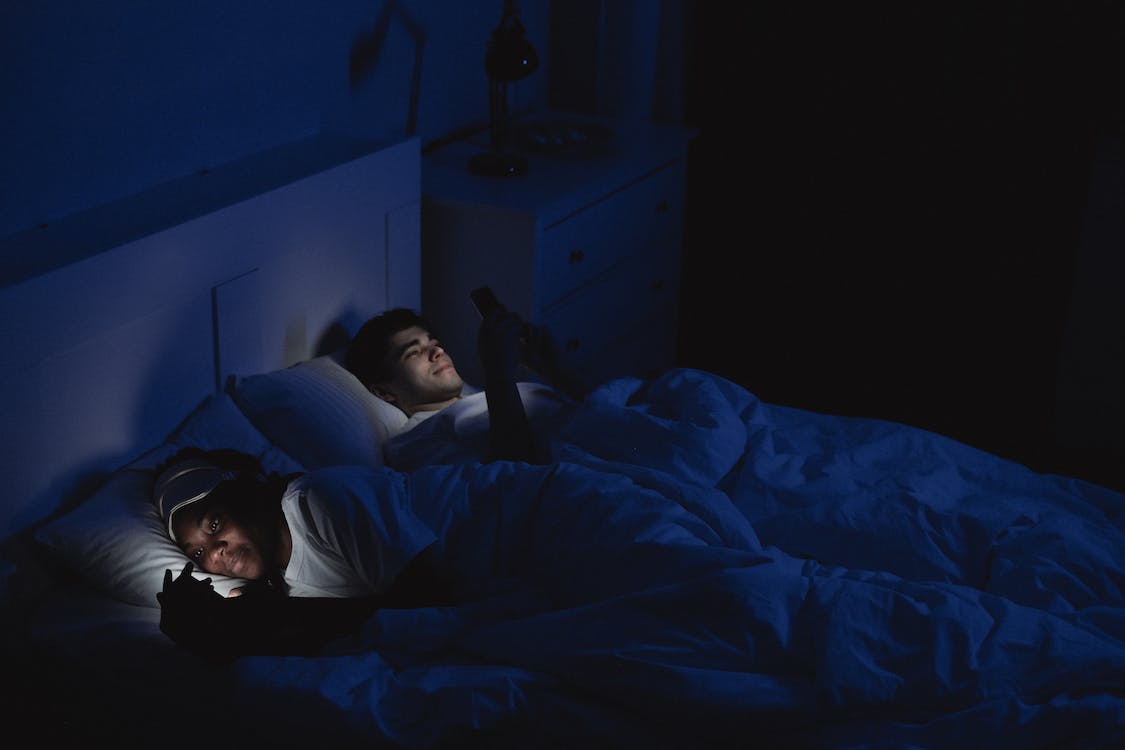 A couple lying in bed and looking at their phones.