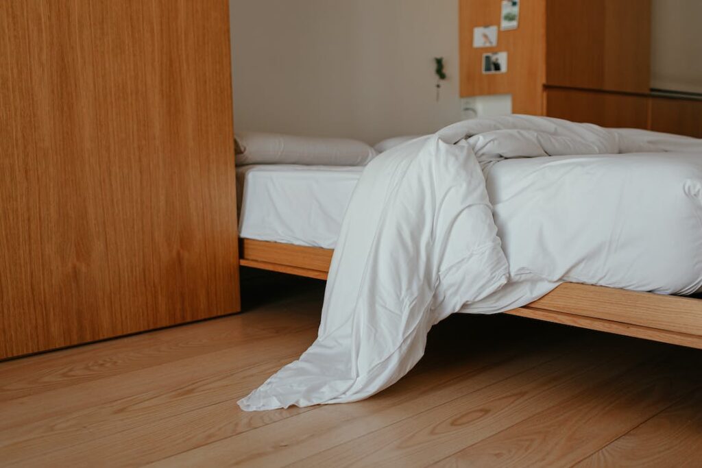 A wooden bed with white sheets next to a wooden wardrobe. 