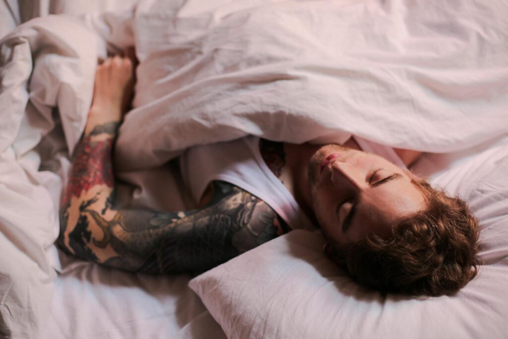 A person with a tattoo sleeve sleeping in a bed